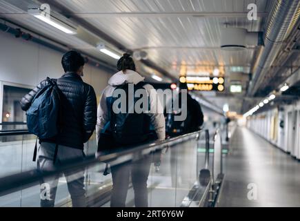 Vue arrière des passagers anonymes hommes et femmes avec des sacs à dos debout sur la passerelle mobile à l'aéroport Banque D'Images