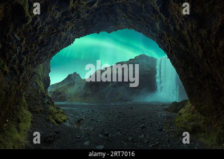 Paysage pittoresque de la grotte de la puissante cascade et des aurores boréales vertes sur les falaises rocheuses à Skogafoss Islande Banque D'Images