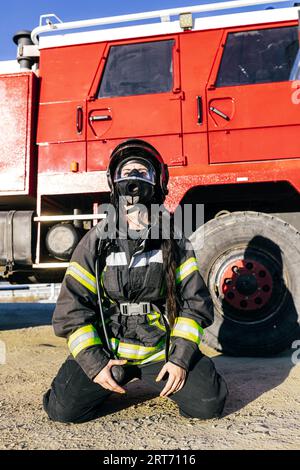 Pompier féminin portant l'uniforme et le masque de protection assis près de la camionnette de pompiers sous le ciel bleu dans la journée ensoleillée Banque D'Images