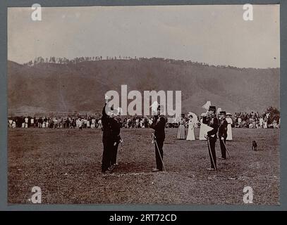 Cérémonie d'assermentation d'un groupe de trois officiers dans un espace ouvert. Un officier prête serment la main levée. Il y a quelques femmes à proximité, plus un public à distance. Sumatra, Indonésie, 1910 Banque D'Images