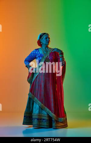 Élégante, mature, belle femme indienne dans des vêtements traditionnels, robe posant sur fond de studio dégradé dans la lumière de néon Banque D'Images