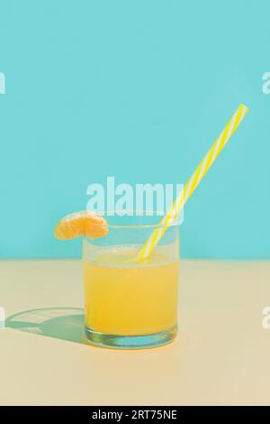 Jus de mandarine dans un verre avec tranche et paille. Fond turquoise et beige. Minimalisme Banque D'Images