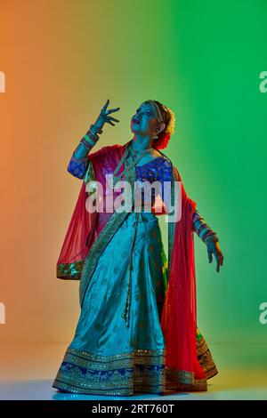 Élégante, mature, belle femme indienne dans des vêtements traditionnels, robe posant sur fond de studio dégradé dans la lumière de néon Banque D'Images