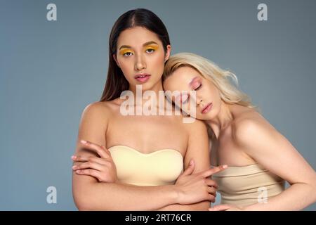 modèles interraciaux avec maquillage des yeux à la mode regardant la caméra sur fond bleu, concept de beauté diverse Banque D'Images