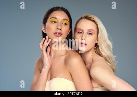 divers jeunes modèles avec maquillage des yeux audacieux posant ensemble sur fond bleu, concept de tendance de beauté Banque D'Images