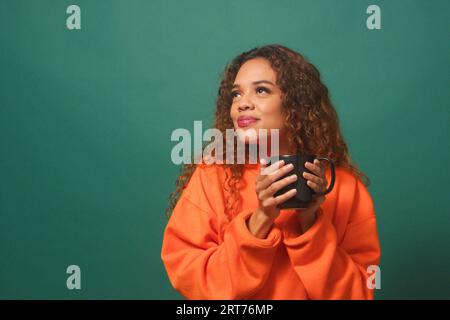 Femme biracial satisfaite sirote une boisson chaude de mug, fond de studio vert Banque D'Images