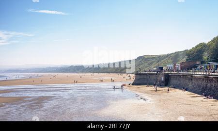 Un mur de mer avec une promenade est d'un côté et les sables s'étendent jusqu'à un promontoire lointain couvert de brume. Les gens sont sur la plage et aussi sur le pr Banque D'Images