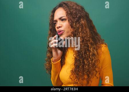 Bouleversée jeune femme parlant sur le téléphone portable, studio vert, bouclé biracial Banque D'Images