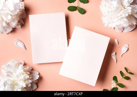Fleurs de pivoine blanches et cartes blanches de voeux sur fond rose poudré, espace de copie. Concept minimal d'invitation de mariage. Banque D'Images