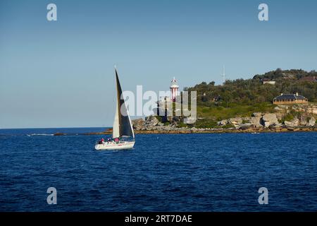 Un petit bateau à voile au large de South Head, le port de Sydney (Port Jackson), le phare historique de Hornby et Lighthouse Keepers Cottage derrière. NSW Australie. Banque D'Images