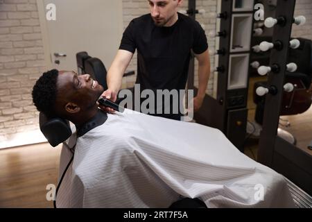 Client afro-américain assis confortablement dans une chaise de barbier Banque D'Images