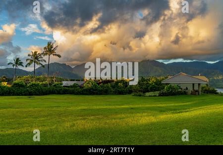 Le lever du soleil illumine les nuages d'orage au-dessus des montagnes Hanalei avec les bâtiments couverts de plantes du 1 Hôtel au premier plan Banque D'Images