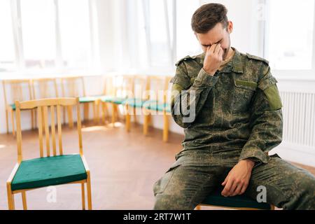 Portrait moyen d'un jeune soldat masculin malheureux en uniforme de camouflage avec SSPT pleurant assis en cercle pendant la séance de thérapie de groupe. Banque D'Images