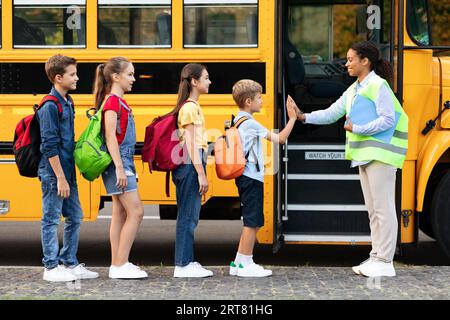 Enseignant en uniforme donnant cinq aux enfants entrant dans le bus scolaire Banque D'Images