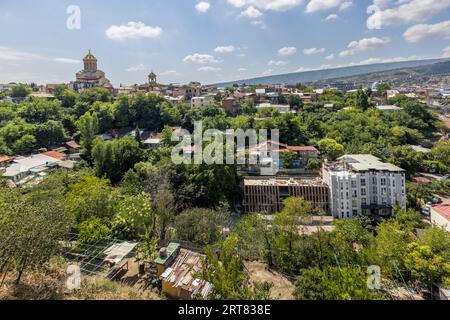 Vue du quartier de Chugureti à Tbilissi, Géorgie. La cathédrale de la Sainte Trinité avec son dôme doré se dresse sur une colline. Les bâtiments résidentiels et les arbres sont visibles. En arrière-plan se trouvent les montagnes Banque D'Images