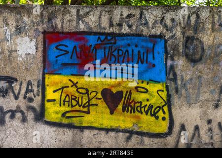 Un graffiti aux couleurs du drapeau ukrainien sur un mur du quartier de Chugureti à Tbilissi, en Géorgie, porte les mots «СЛАВА УКРАЇНІ!» En français : « Gloire à l'Ukraine ! ». Une couronne est dessinée au-dessus des inscriptions. Le champ jaune contient le tag « Tabu92 », un cœur rouge foncé et le mot « Ukraine ? ». En 2023, des graffitis contre la Russie et en faveur de liens plus étroits avec l'Europe ont façonné le paysage urbain de Tbilissi. Banque D'Images