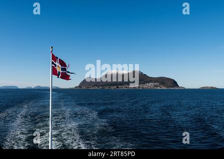 Un message norvégien ou un drapeau postal a été hissé sur le poste du mailboat agitant dans le vent avec la mer ouverte et les montagnes sur jour d'hiver ensoleillé Banque D'Images