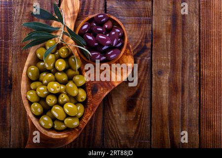 Olives vertes et noires en bois d'anciennes coupes sur fond de bois. Vue de dessus avec l'espace pour le texte Banque D'Images