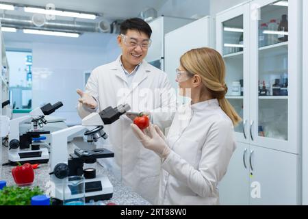 Jeunes scientifiques et scientifiques, collègues asiatique homme et femme travaillent en laboratoire sous microscopes, étude et recherche alimentaire. Ils sourient et discutent des résultats. Banque D'Images