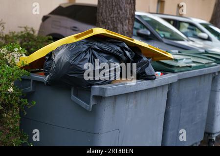 Une poubelle grise remplie de déchets, surmontée d'un couvercle jaune. Banque D'Images