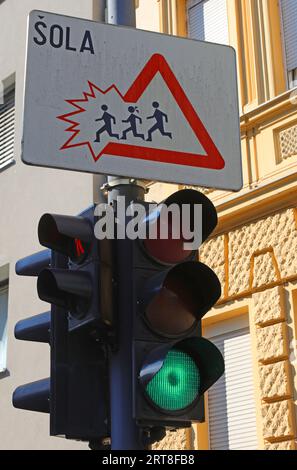Panneau routier avec les enfants sortant du triangle et le feu de circulation et le texte qui signifie ÉCOLE en slovène Banque D'Images