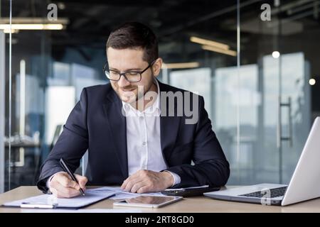 Jeune homme d'affaires travaillant au bureau sur le lieu de travail avec des documents, signant un accord, travaillant avec des comptes Banque D'Images