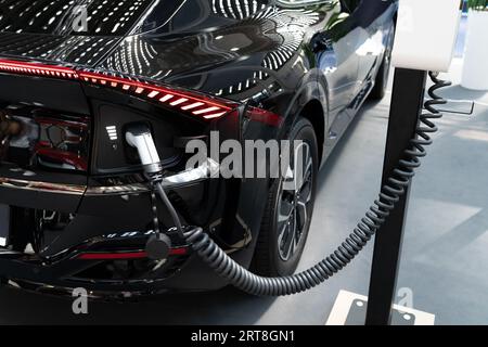 Gros plan d'une voiture électrique avec un câble connecté et une borne de recharge. Banque D'Images