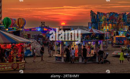 funfair lumineux avec des promenades sur la plage en face d'un beau coucher de soleil de ciel rouge à st annes sur la mer festival international de cerf-volant 2023 Banque D'Images