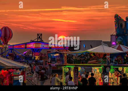 funfair lumineux avec des promenades sur la plage en face d'un beau coucher de soleil de ciel rouge à st annes sur la mer festival international de cerf-volant 2023 Banque D'Images