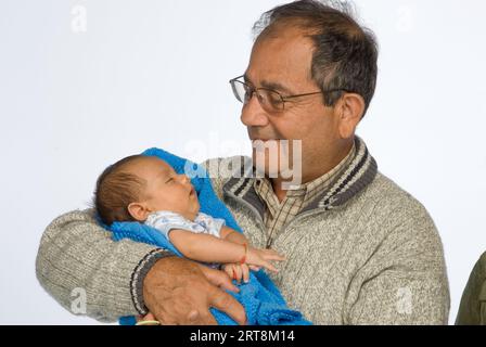 Photo de studio d'un homme hispanique tenant un bébé dans une couverture bleue, probablement son petit-fils Banque D'Images