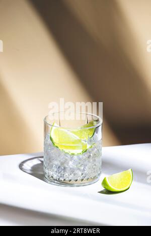 Cocktail TI punch avec rhum agricole blanc, sirop de sucre et citron vert, boisson traditionnelle des Caraïbes. Fond beige, feuilles de palmier ombre, copie spac Banque D'Images