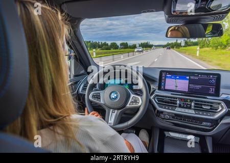 Belle vue de femme conduisant la nouvelle BMW iX3 M Sport noir voiture électrique modèle sur autoroute. Suède. Banque D'Images