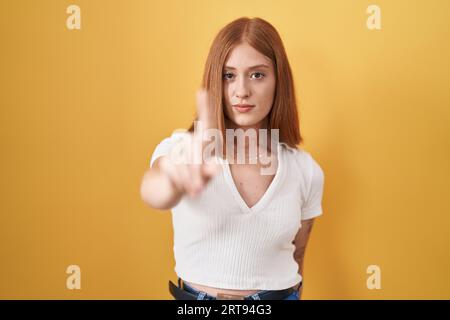 Jeune femme rousse debout sur fond jaune pointant avec le doigt vers le haut et l'expression en colère, ne montrant aucun geste Banque D'Images