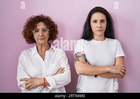 Mère hispanique et fille portant un t-shirt blanc décontracté sur fond rose sceptique et nerveux, désapprouvant l'expression sur le visage avec les bras croisés. Banque D'Images
