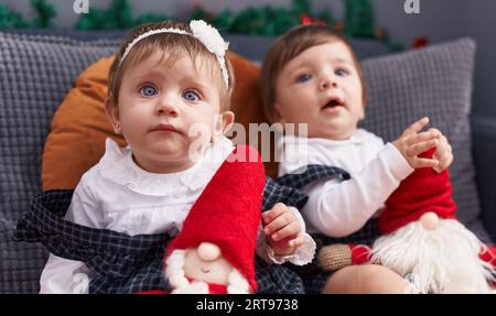 Deux adorables bébés assis sur le canapé jouant avec la poupée du père noël à la maison Banque D'Images