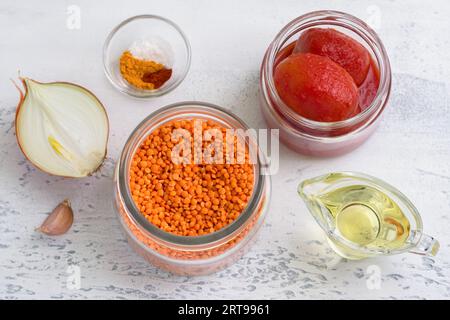 Ingrédients pour sauce tomate végétalienne aux lentilles, soupe ou crêpes aux lentilles : lentilles rouges, oignons, ail, tomates en conserve, épices et huile végétale sur li Banque D'Images