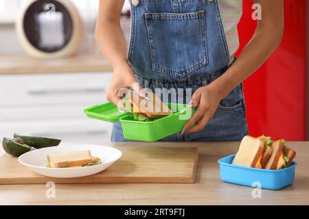 Jeune femme mettant le sandwich dans la boîte à lunch de l'école à la maison Banque D'Images