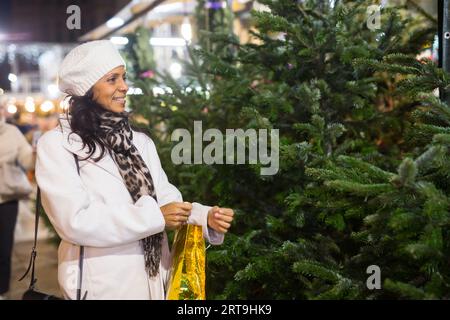 Femme latino-américaine souriante qui choisit le sapin pour la fête du nouvel an à la foire de rue Banque D'Images