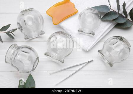 Ensemble de ventouses, gua sha et branches d'eucalyptus sur table en bois blanc, pose plate Banque D'Images