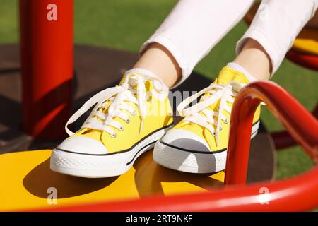 Femme dans les baskets classiques jaunes Old School sur le carrousel à l'extérieur, closeup Banque D'Images