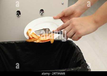 Femme jetant des pommes de terre cuites avec du ketchup dans la poubelle à l'intérieur, gros plan Banque D'Images