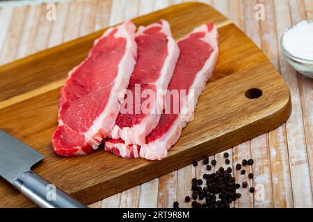 Entrecôtes de bœuf cru avec du poivre sur une surface en bois Banque D'Images