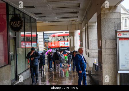 LONDRES - 24 avril 2023 : les Londoniens cherchent un abri de la pluie près de la gare de Charing Cross, avec l'emblématique bus à impériale rouge londonien dans le Banque D'Images