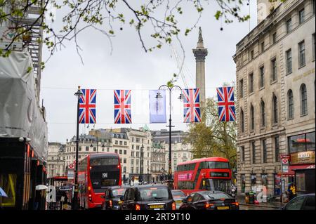 LONDRES - 24 avril 2023 : taxis noirs classiques et bus à impériale rouges de Londres sous les drapeaux de l'Union Jack avec la colonne Nelson et Trafalgar Square Banque D'Images