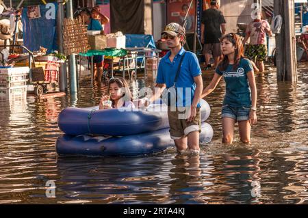 Des réfugiés climatiques, un père, une mère et une fille, pataugent dans les eaux de crue (la fille fait du radeau) sur Phahon Yothin Road, Bangkok, Thaïlande. © Kraig Lieb Banque D'Images