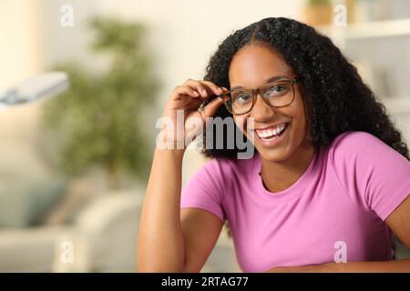 Heureuse femme noire portant des lunettes regarde la caméra à la maison Banque D'Images