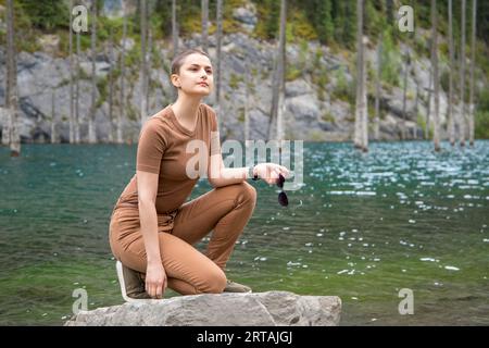 Jeune femme voyage à travers les montagnes Tien Shan en Asie centrale, posant sur une pierre avec en toile de fond le pittoresque lac de montagne Kaindi In Banque D'Images