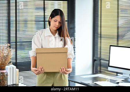 Employée frustrée tenant une boîte en carton avec des effets personnels, quittant le bureau après avoir quitté un emploi Banque D'Images