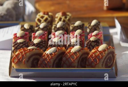 Présentoir à pâtisserie avec variations de gâteaux crus sans cuisson, tranches de roulade décorées d'un treillis de chocolat ou de crème de fruits et recouvertes d'amandes blanchies Banque D'Images