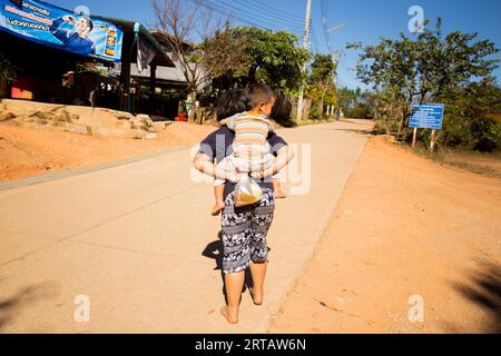 Chiang Mai, Thaïlande ; 1 janvier 2023 : une femme portant un enfant sur le dos et un sac de nourriture dans un village dans les montagnes de Chiang Mai. Banque D'Images